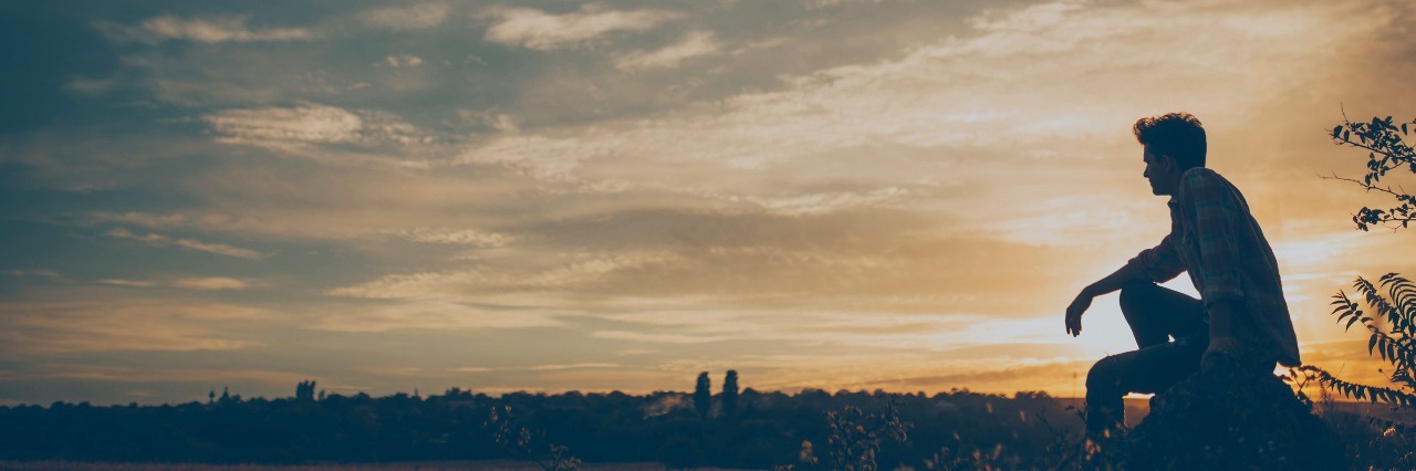 The Challenges of Being a Man and Living With Lyme Disease and Anxiety Silhouette of young man sitting on sunset or sunrise. Confident teenage boy thinking on cliff stone.