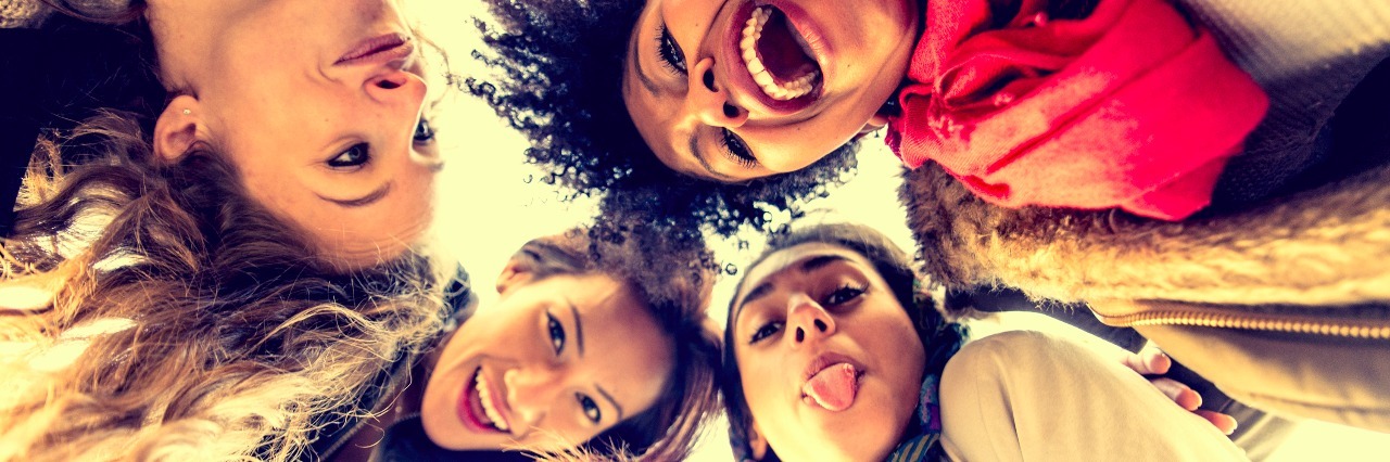 Group of young women hugging in a circle - Four students smiling at camera - Best friends spending time together