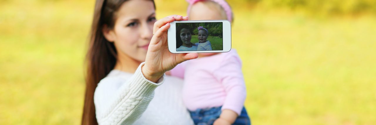 Mother and baby taking self-portrait on smartphone in sunny summer