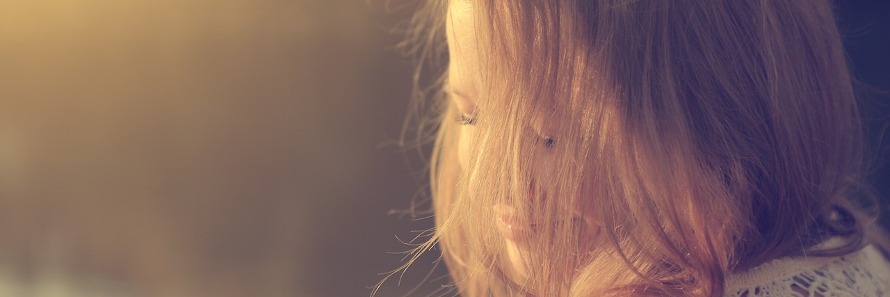 Why My Anxiety Means That I Can't Shut My Emotions Out woman sitting by a lake in the sunlight