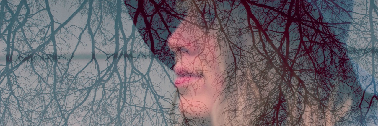 An in camera double exposure of a woman with long hair wearing a fedora hat and upside down trees.