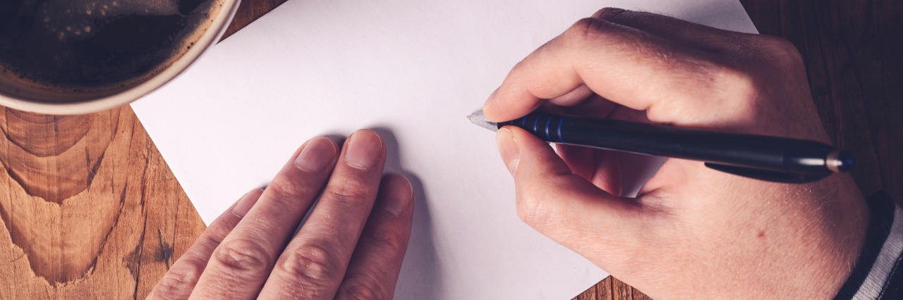 Letter to Loved Ones About Life With Fibromyalgia woman writing a letter on a desk next to mug of coffee