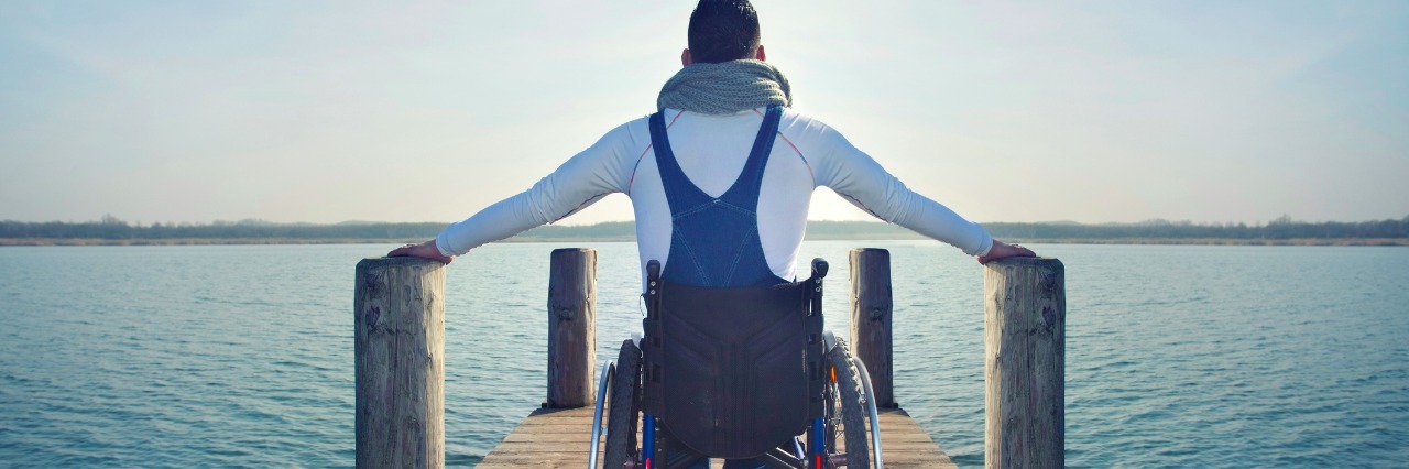disabled Young man in wheelchair on a boardwalk on lake enjoying the view