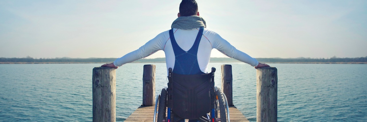 Toad&Co Hires & Sends People With Disabilities on Accessible Vacations disabled Young man in wheelchair on a boardwalk on lake enjoying the view