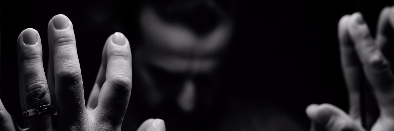 Dealing With Anger When You Have Chronic Fatigue Syndrome Man in despair with raised hands and bowed head, monochromatic image in a low light room looking in front of mirror