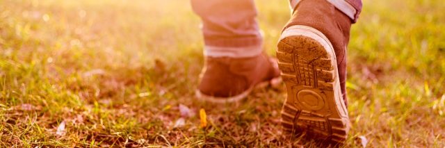 Close-up of person's legs and shoes walking on muddy grass