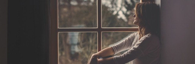 woman sitting in a windowsill looking out at a cloudy sky