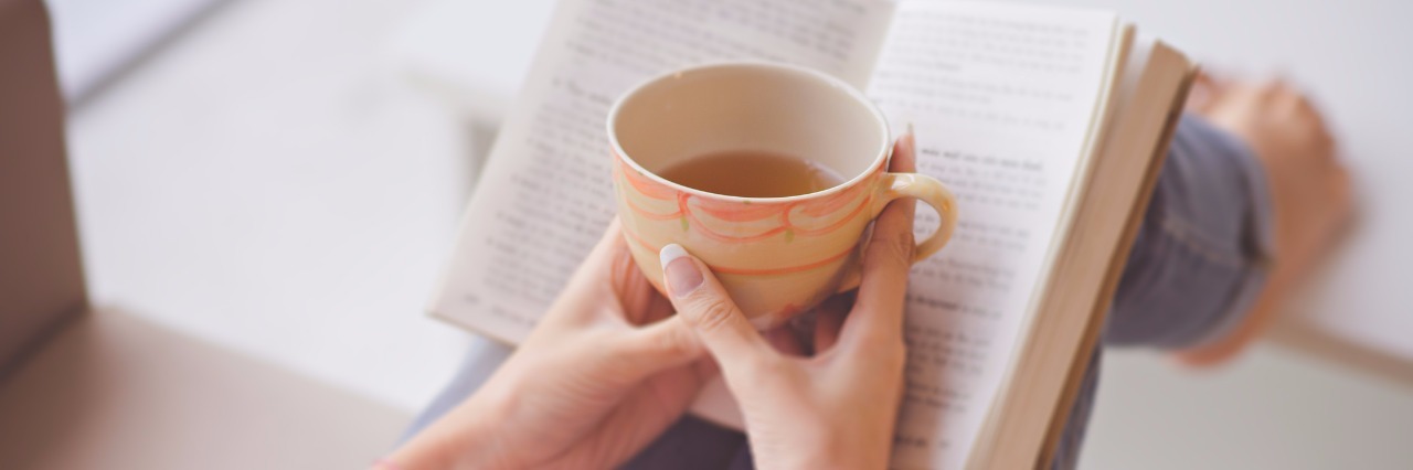Close-up of female hands holding teacup in front of opened book