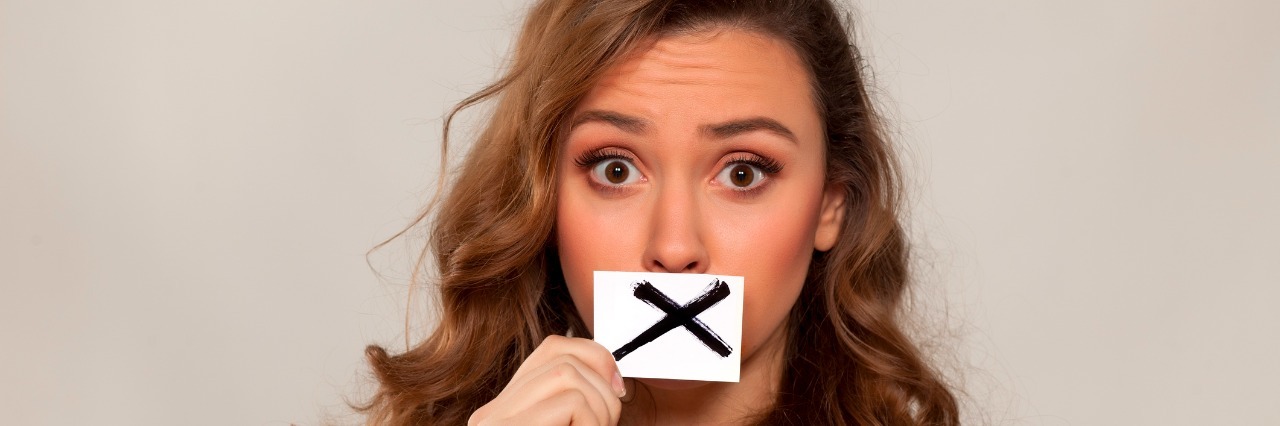 shocked young girl with X sign drawn on paper over her mouth