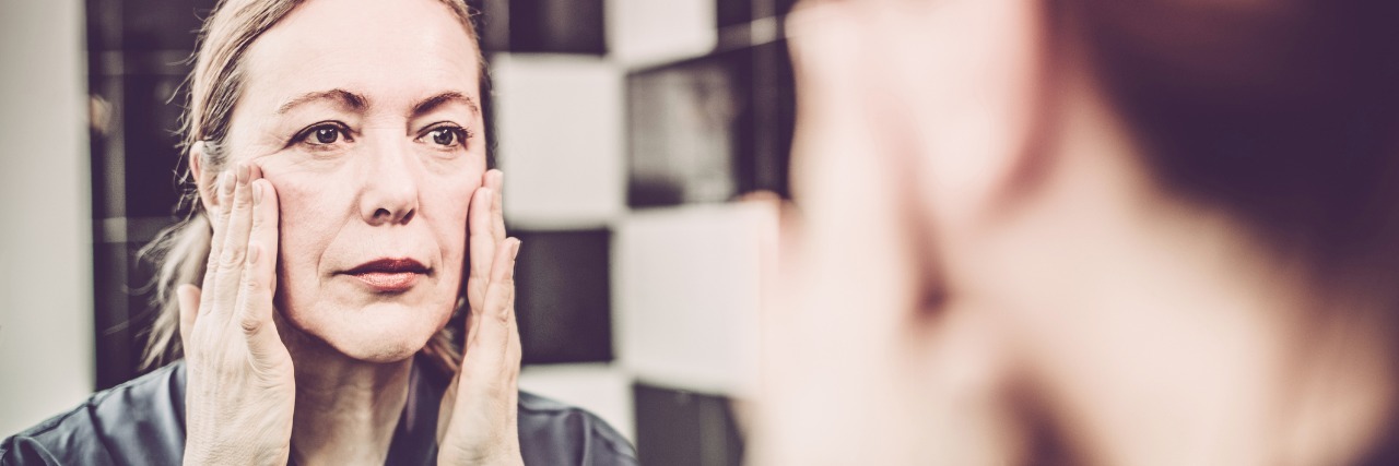 Lupus, Kidney Disease: Challenges of Illness Being Invisible woman looking at herself in the mirror with her hands on her cheeks