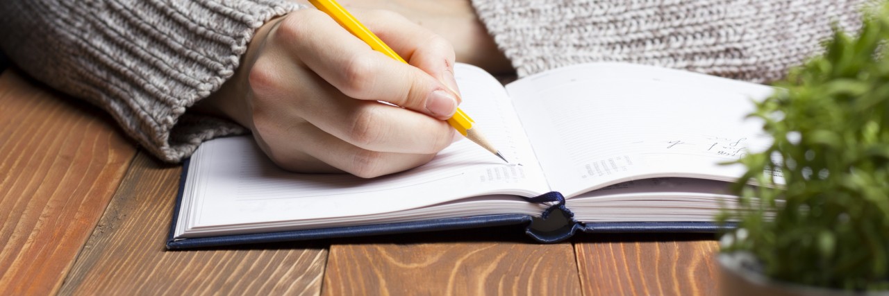 A Letter to Anxiety female hands with pencil writing on notebook.