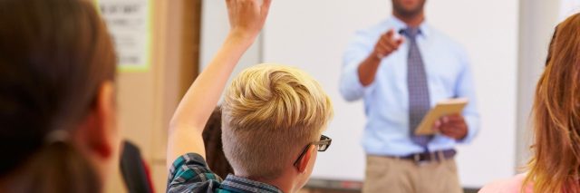 Kids in classroom raising hands with teacher calling on student