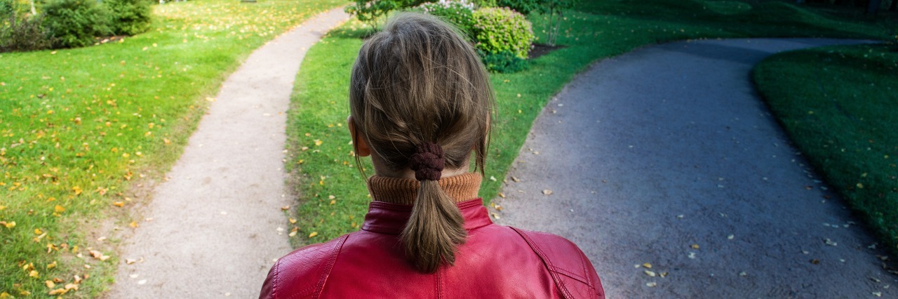 Making Choices About When to Fight Fibromyalgia, Chronic Pain woman in red coat standing at a fork in the road