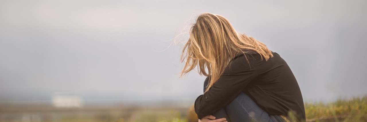I Can't Go to Funerals Because of My Misophonia Side view of a despaired woman sitting curled up in nature.
