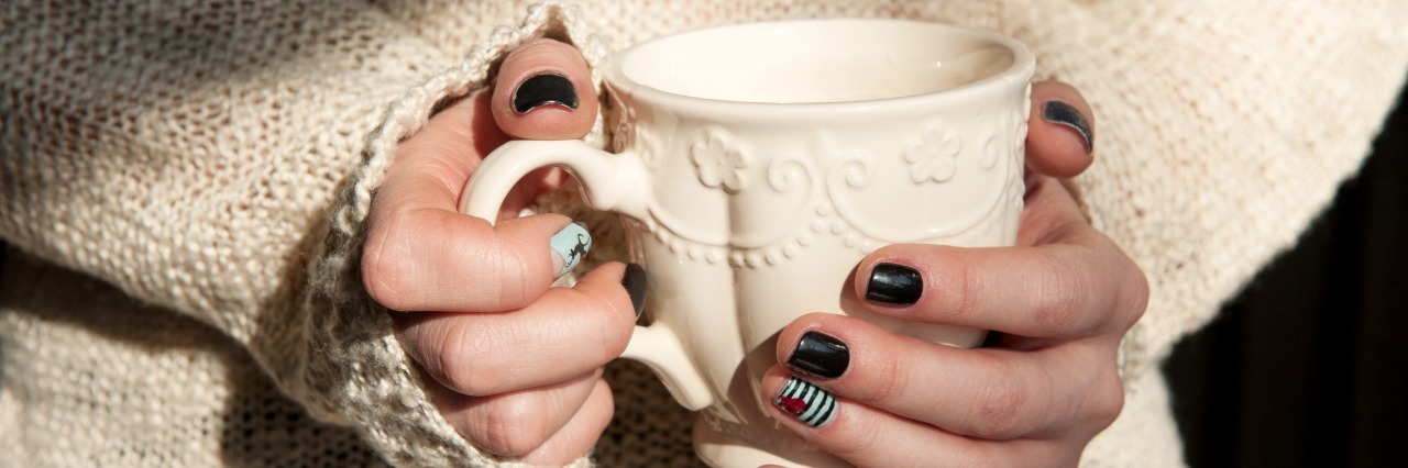 woman wearing a sweater and holding a white mug with painted fingernails