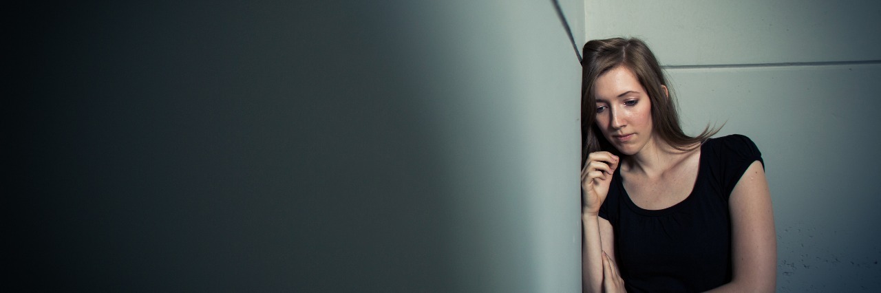 What It's Like to Live With Both Anxiety and Depression young woman leaning against wall harsh lighting depression