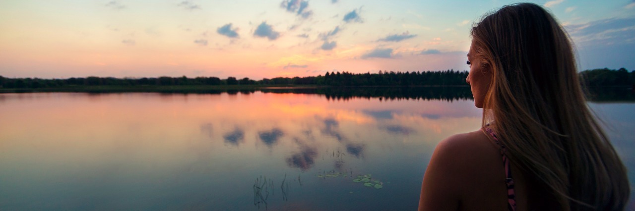 Things to Know During Multiple Sclerosis Awareness Month Beautiful woman looking across a pristine and calm lake at a gorgeous sunset. Copy space