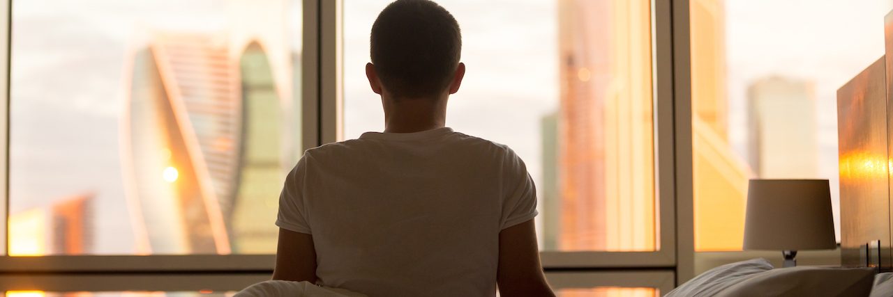 How Therapy Helped Me With Suicidal Thoughts, Self-Harm and Anxiety Man sitting in bed, looking out a window