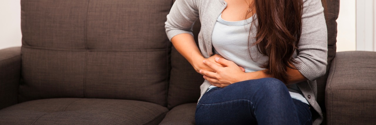 What It's Like Living With Gastrointestinal Problems and Gastroparesis brunette from stomach ache while sitting in a sofa