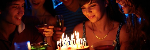 girl blowing out candles on a birthday cake surrounded by friends