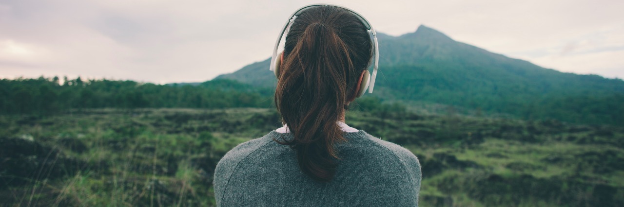 Woman in headphones listening music in nature and at the mountain