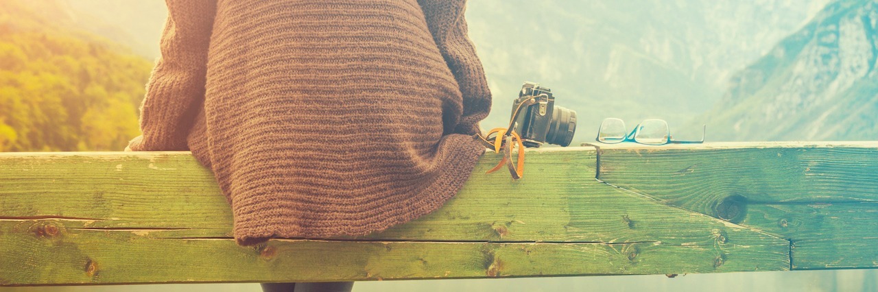 What Self-Care Really Means for Mental Illness Girl sitting on a wooden pier near water.