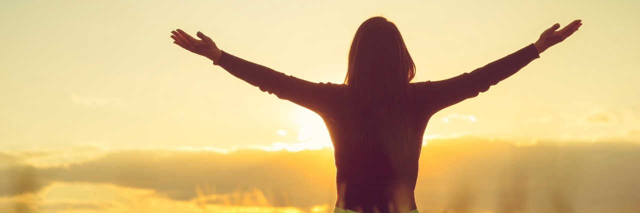 woman in field with sunset spreading arms wide feeling free
