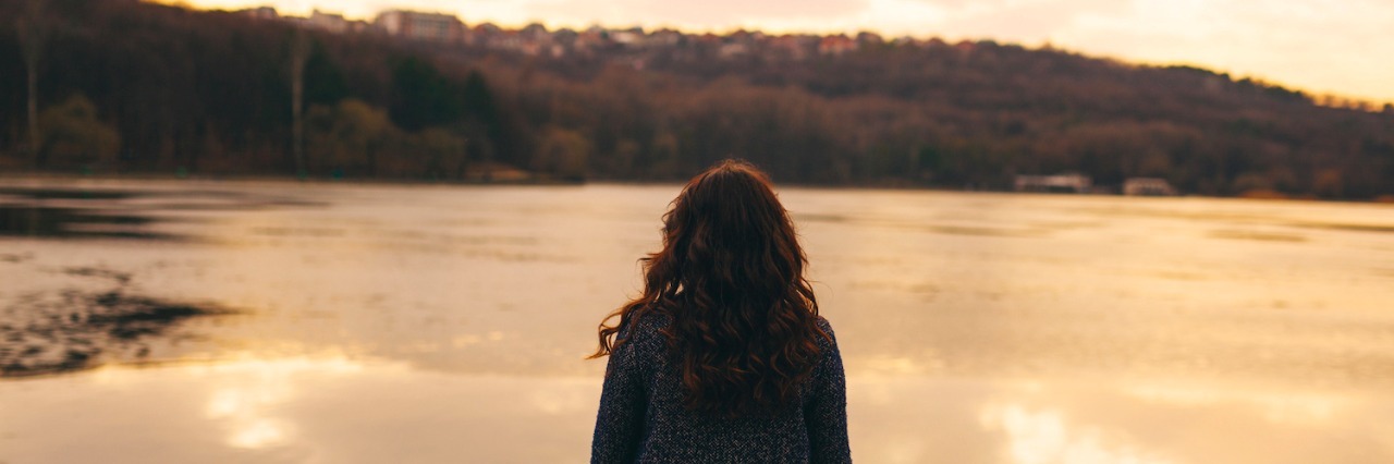 Having an Undiagnosed Seizure Disorder and Waiting for a Diagnosis Woman wearing jacket, standing near lake at sunset