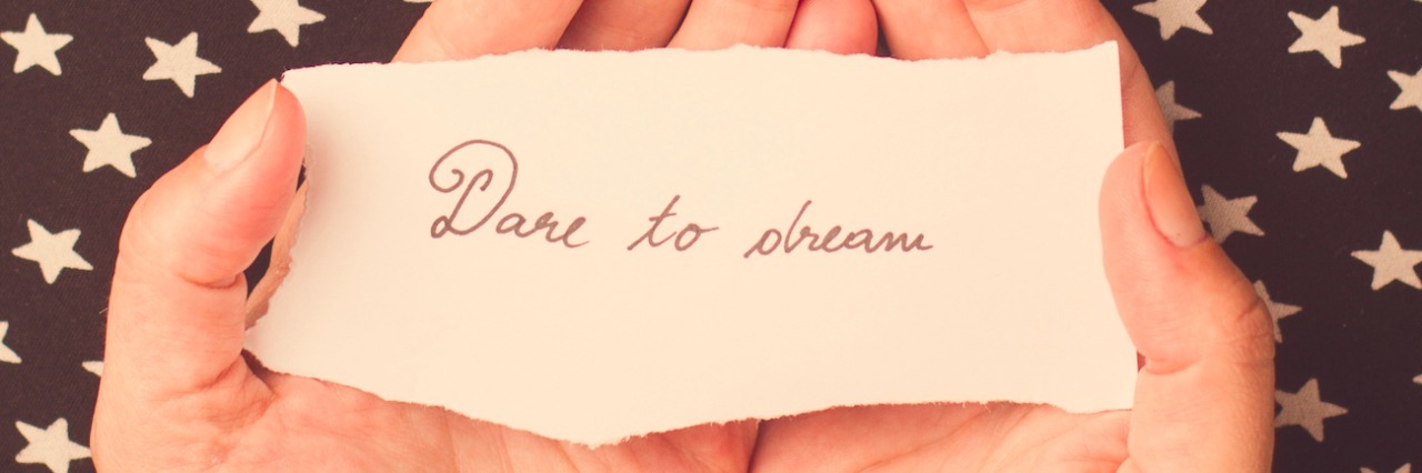a piece of paper that says [dare to dream] on palms of someone's hands, with a star background