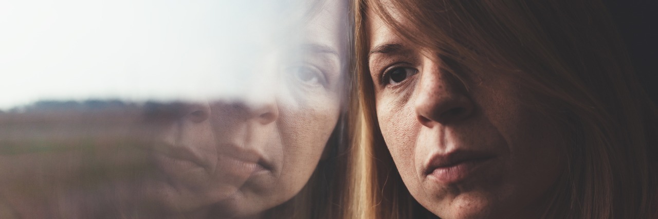 What 'I'm Just Tired' Means for Someone With Chronic Illness woman leaning against a window and looking unhappy