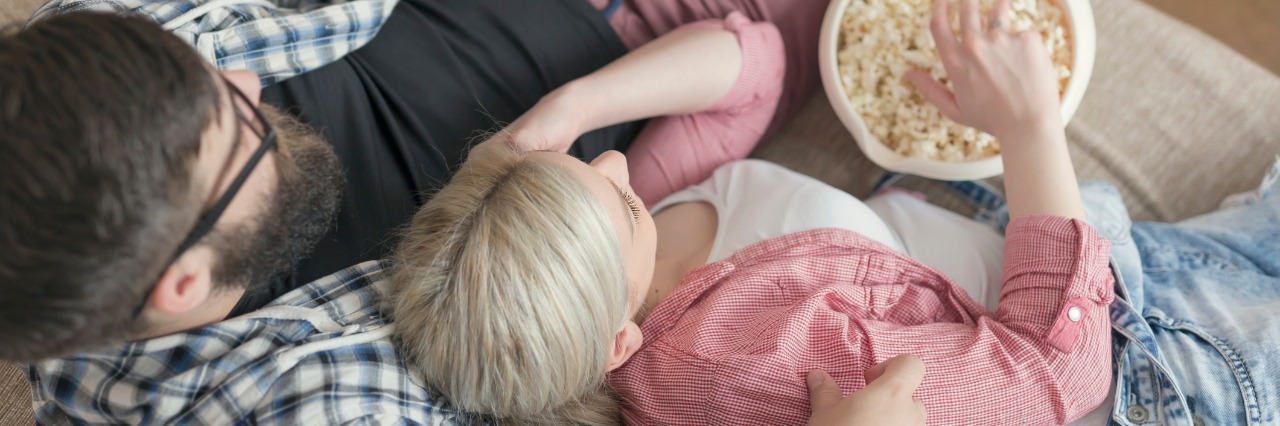 Maintaining a Home When You Have Fibromyalgia man and woman laying on couch, eating popcorn, and watching tv