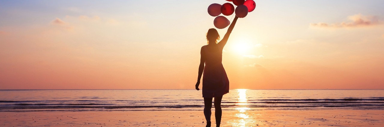 woman on beach at sunset holding balloons