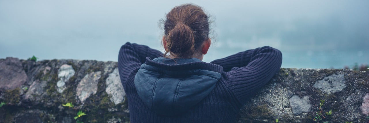 Why Being Called a Burden Is an Insult to Those with Illness A young woman is resting on a wall outside in the mist