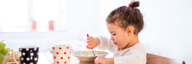 Girl sitting at table in kitchen, eating breakfast