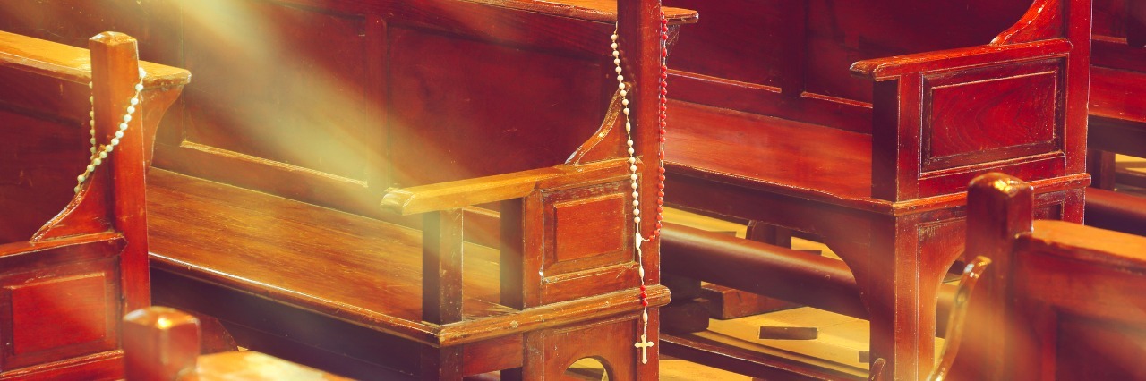 wooden church pews in church and rosary beads with sunlight
