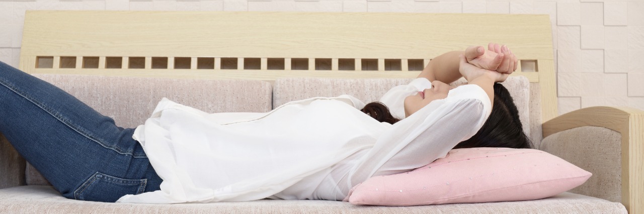 Daily Thoughts and Worries About Life With Crohn's Disease woman laying on her couch with her arms crossed over her head