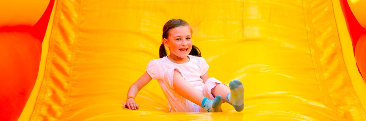 Parenting a Child With Cri Du Chat: Climbing 'the Giant Slide' Happy little girl having lots of fun on a jumping castle while sliding.