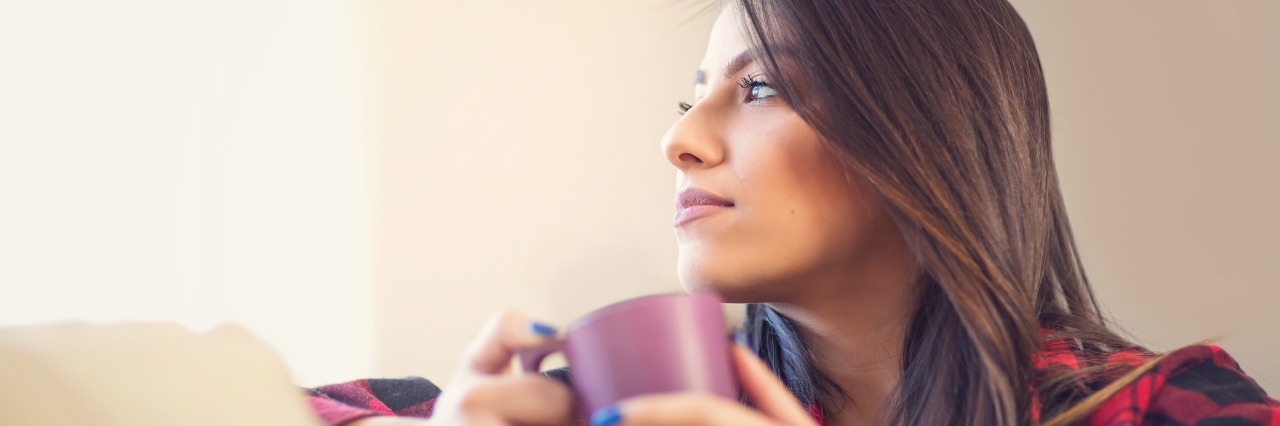 What to Know About Your Future With Chronic Illness woman holding mug and sitting on her couch looking off into the distance