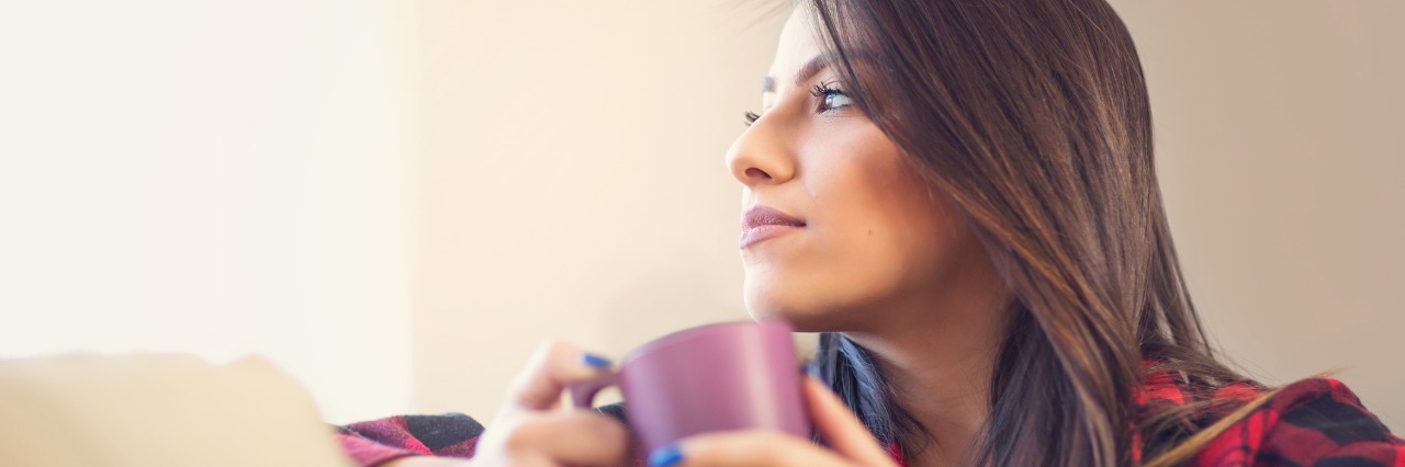 woman holding mug and sitting on her couch looking off into the distance