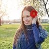 woman smiling outside in a park with a red flower in her hair