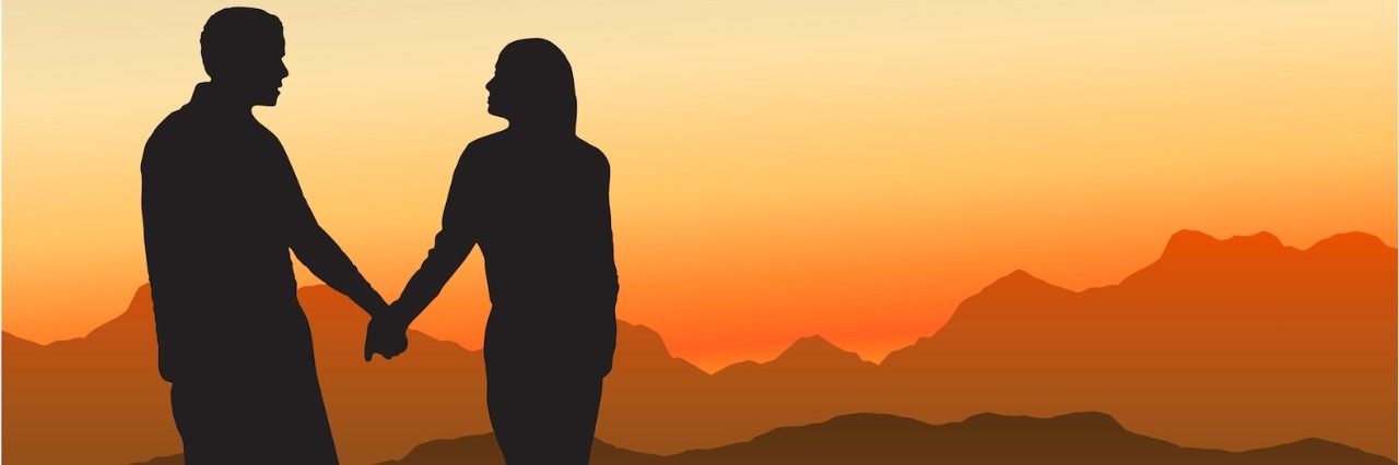 Silhouette of couple holding hands in front of mountain landscape at sunset