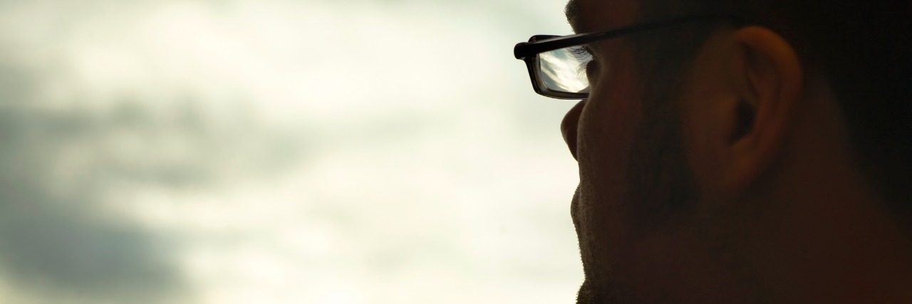 Profile of man wearing glasses, looking toward clouds in sky