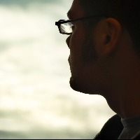 Profile of man wearing glasses, looking toward clouds in sky