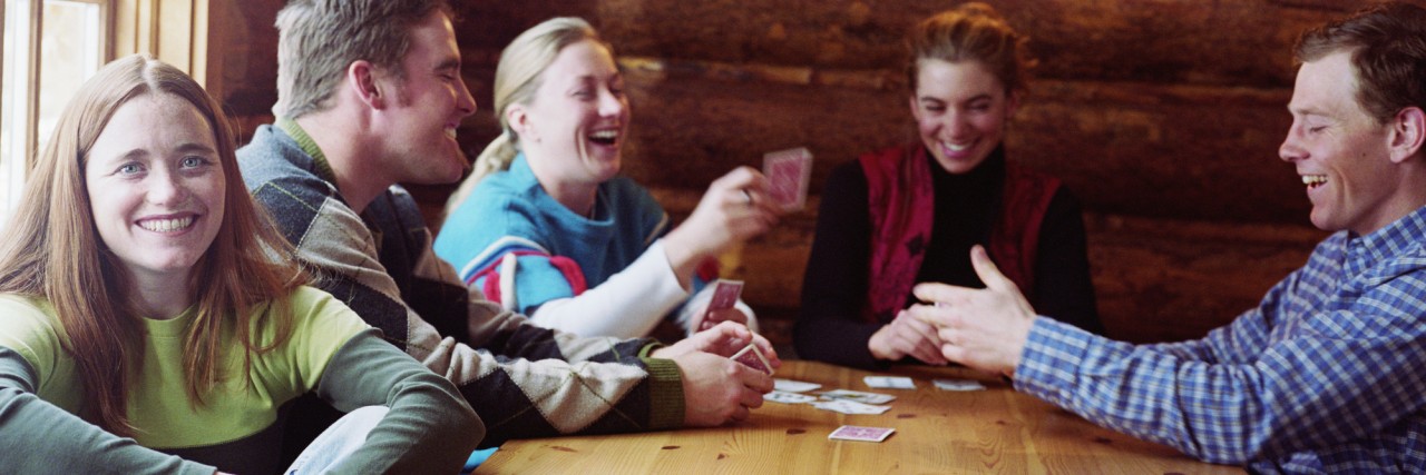 Group of young adults playing cards in log cabin, laughing