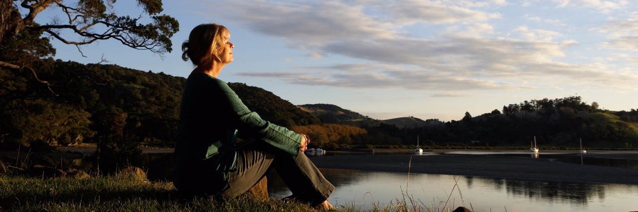 older woman sitting next to a lake at sunset in quiet contemplation