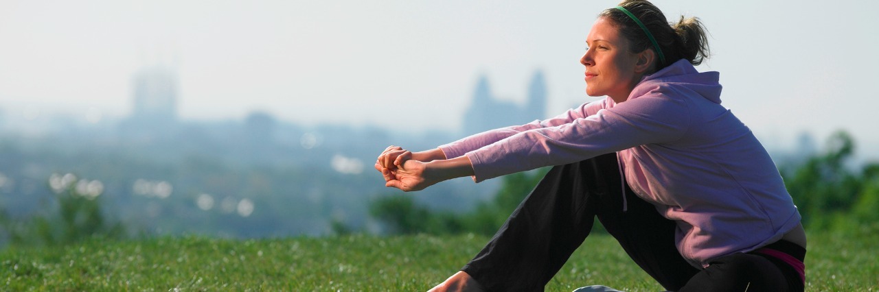 The Moment I Realized I Need to Fully Accept My Rosacea Young woman sitting on grass in sport clothes, cityscape in background