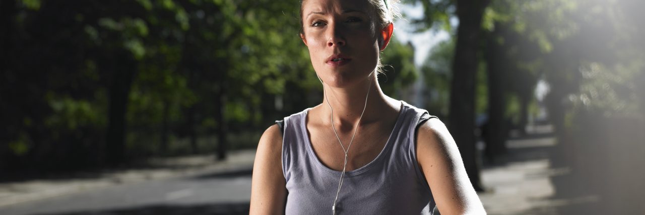 Why I Continue to Be a Runner With Chronic Pain Conditions Young woman jogging on street with mp3 player, checking time
