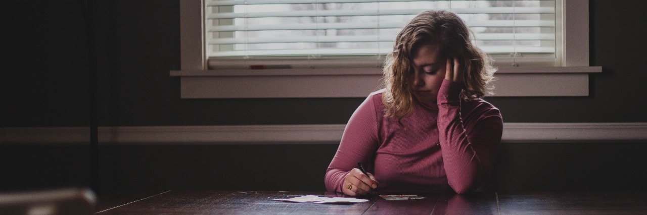 girl in pink sweater writing at a dark wood table