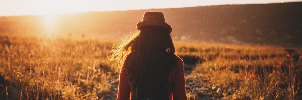 The Importance of Closely Managing Your Mental Illness Recovery woman in a field at sunset facing away from camera