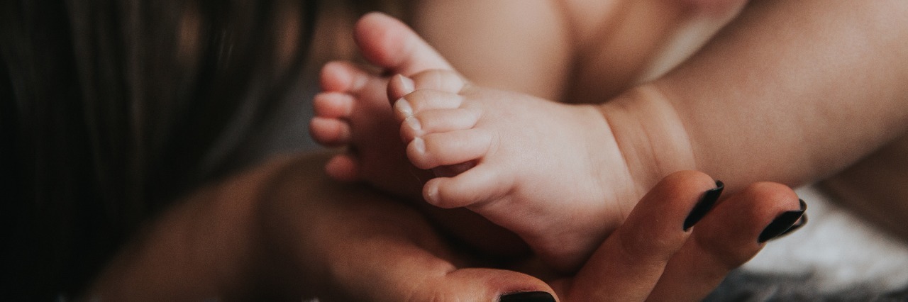 mother's hand with nail polish holding baby feet